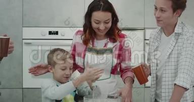 可爱的一家人一起准备早餐，小男孩在现代厨房里用手搅拌器混合所有的配料